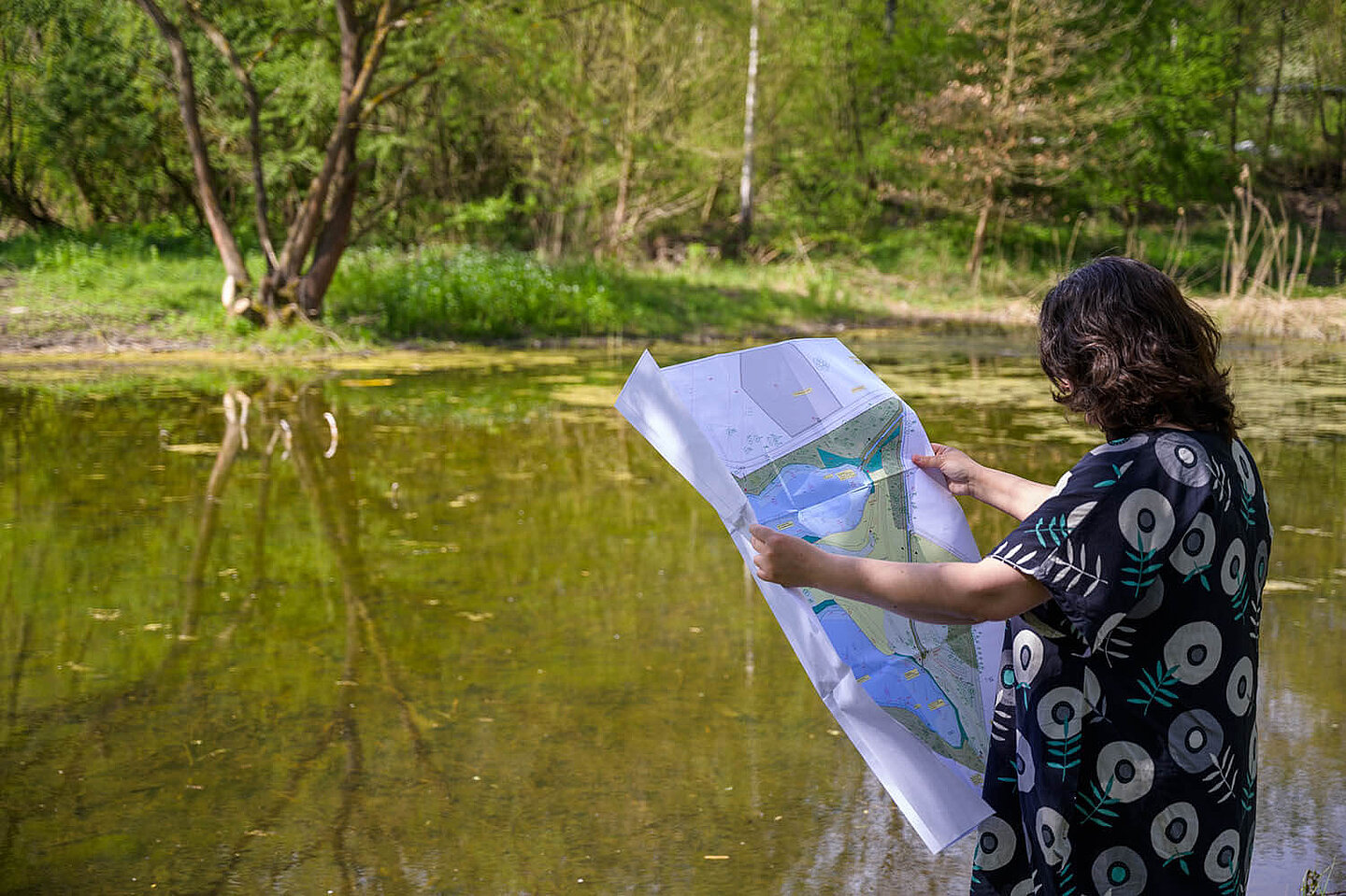 a person standing in front of a pond is holding a construction plan of the ponds