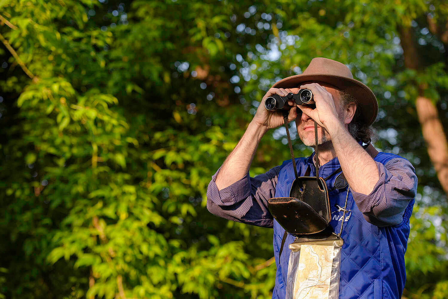 ein in der Natur stehender Mann sieht mit dem Fernglas in die Ferne