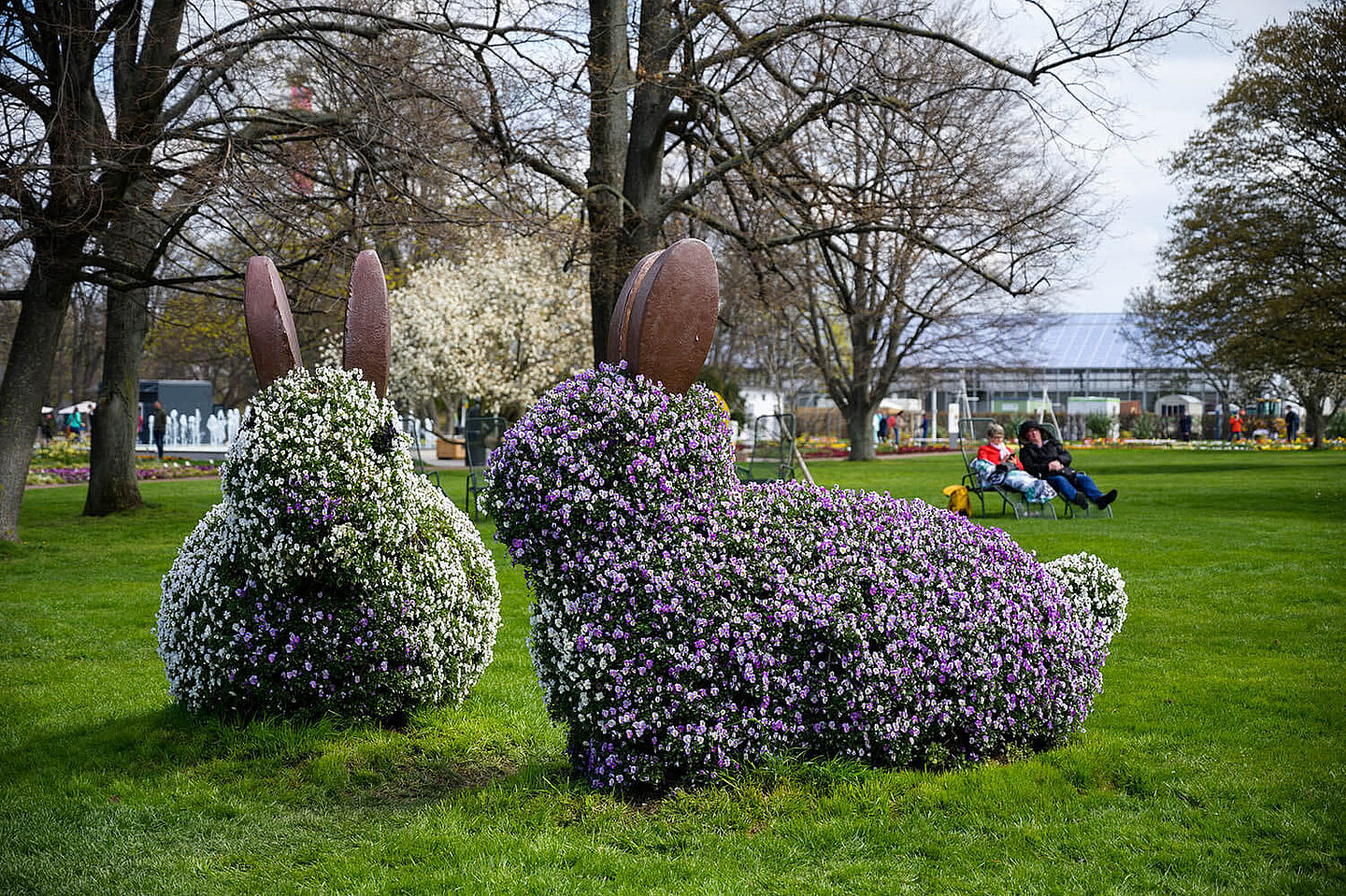 Hasenfiguren aus Blumen. Im Hintergrund Menschen auf Liegestühlen auf einer Wiese
