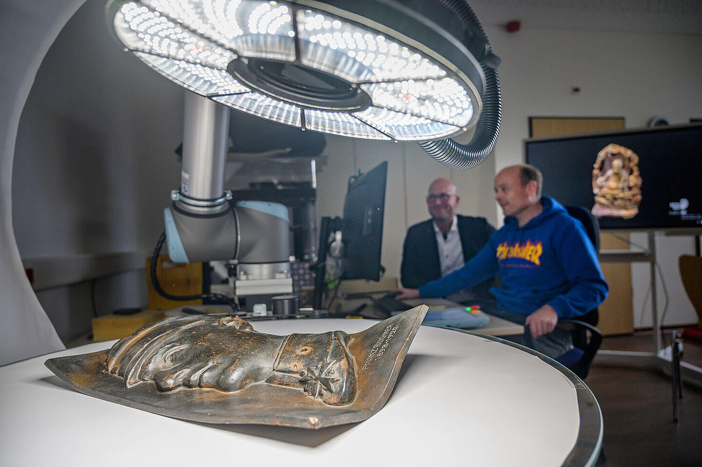  Two men look at a brightly lit bronze sculpture through their monitor