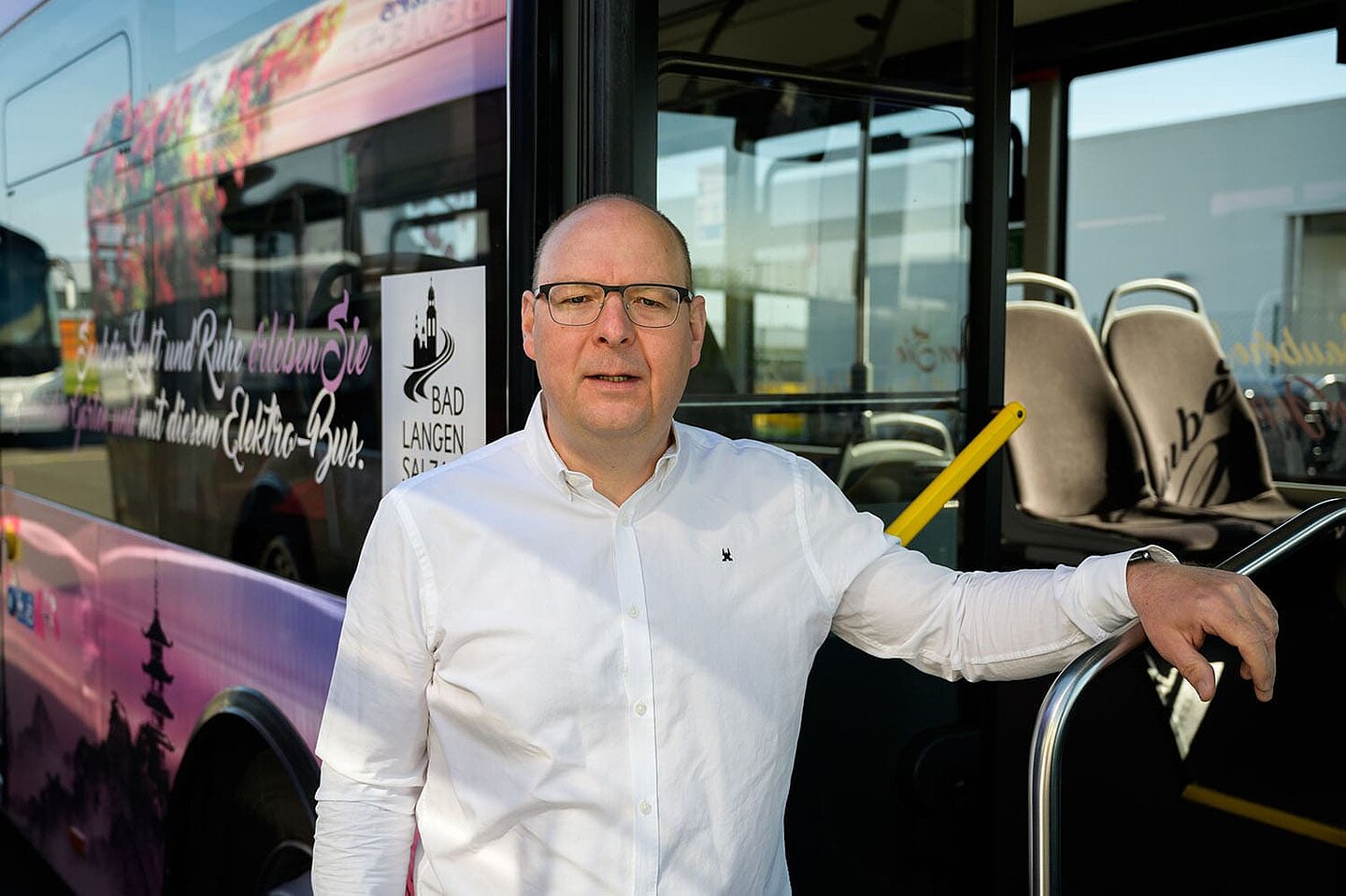 Ein Busfahrer in einem weißen Hemd steht vor seinem Tourbus