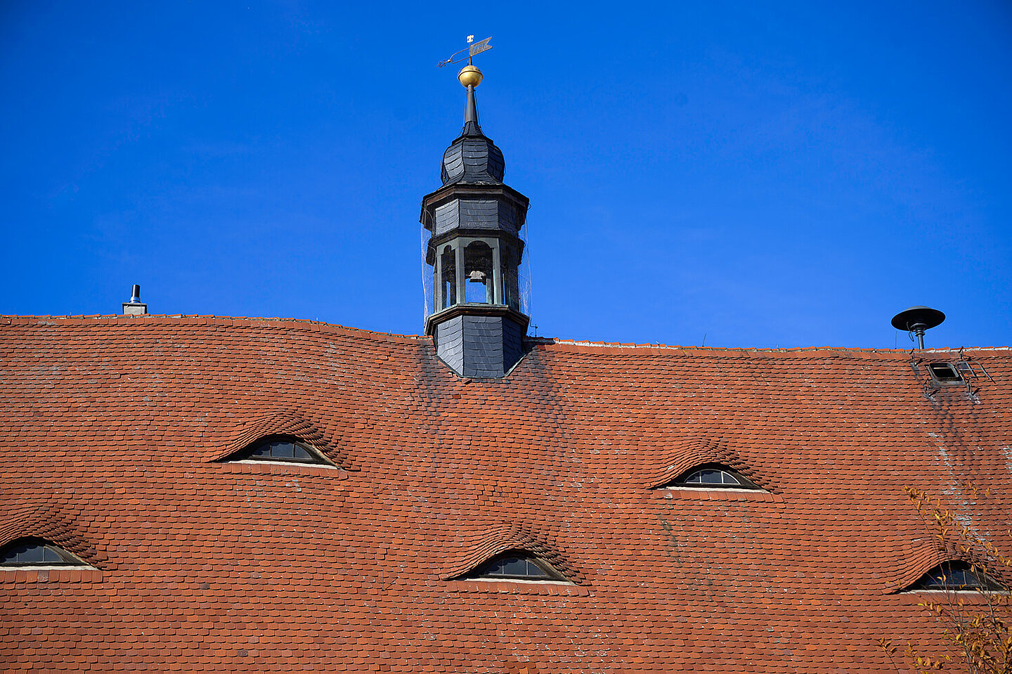 Bell tower of the Buttstadt town hall. This one sits on a red roof with small windows. An alarm siren is mounted in a corner