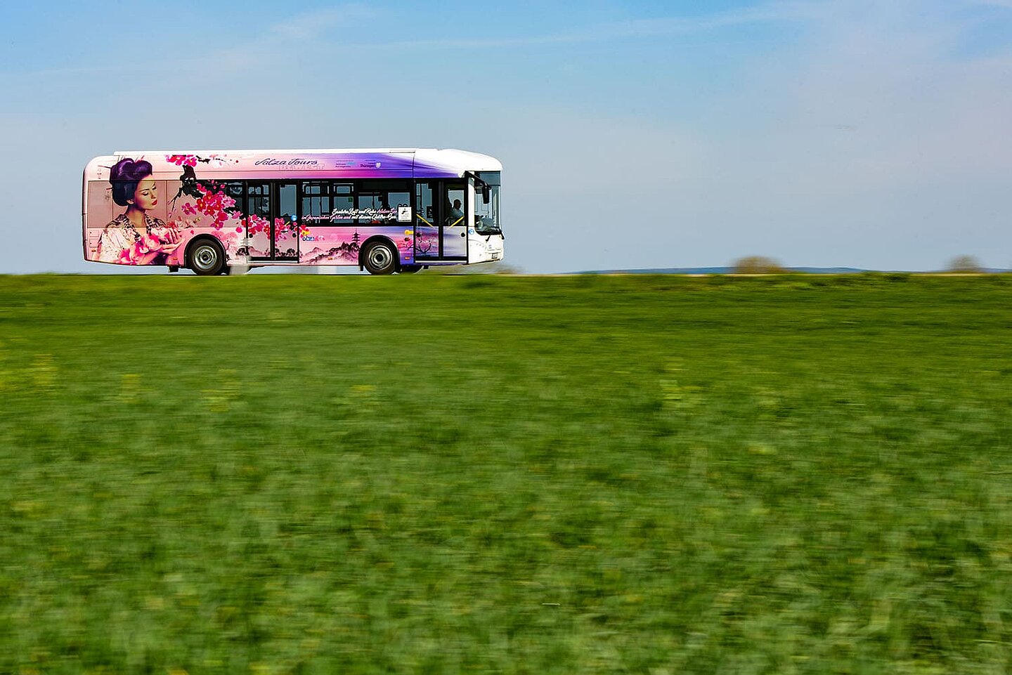 Ein mit Blumen bedruckter Bus fährt vorbei an einer grünen Wiese